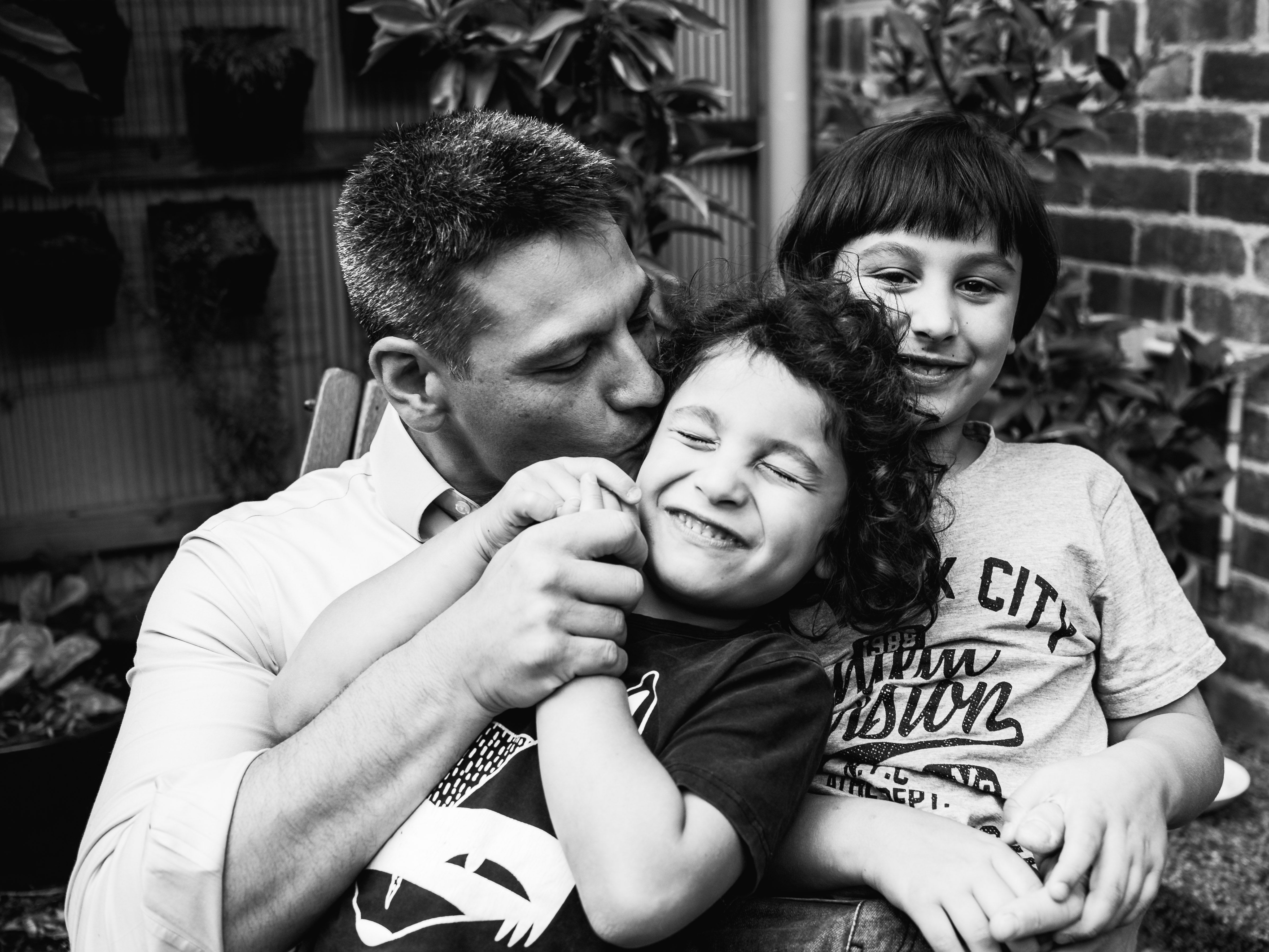 photograph of a father kissing his youngest son in their backyard in Carlton North, Melbourne, Australia