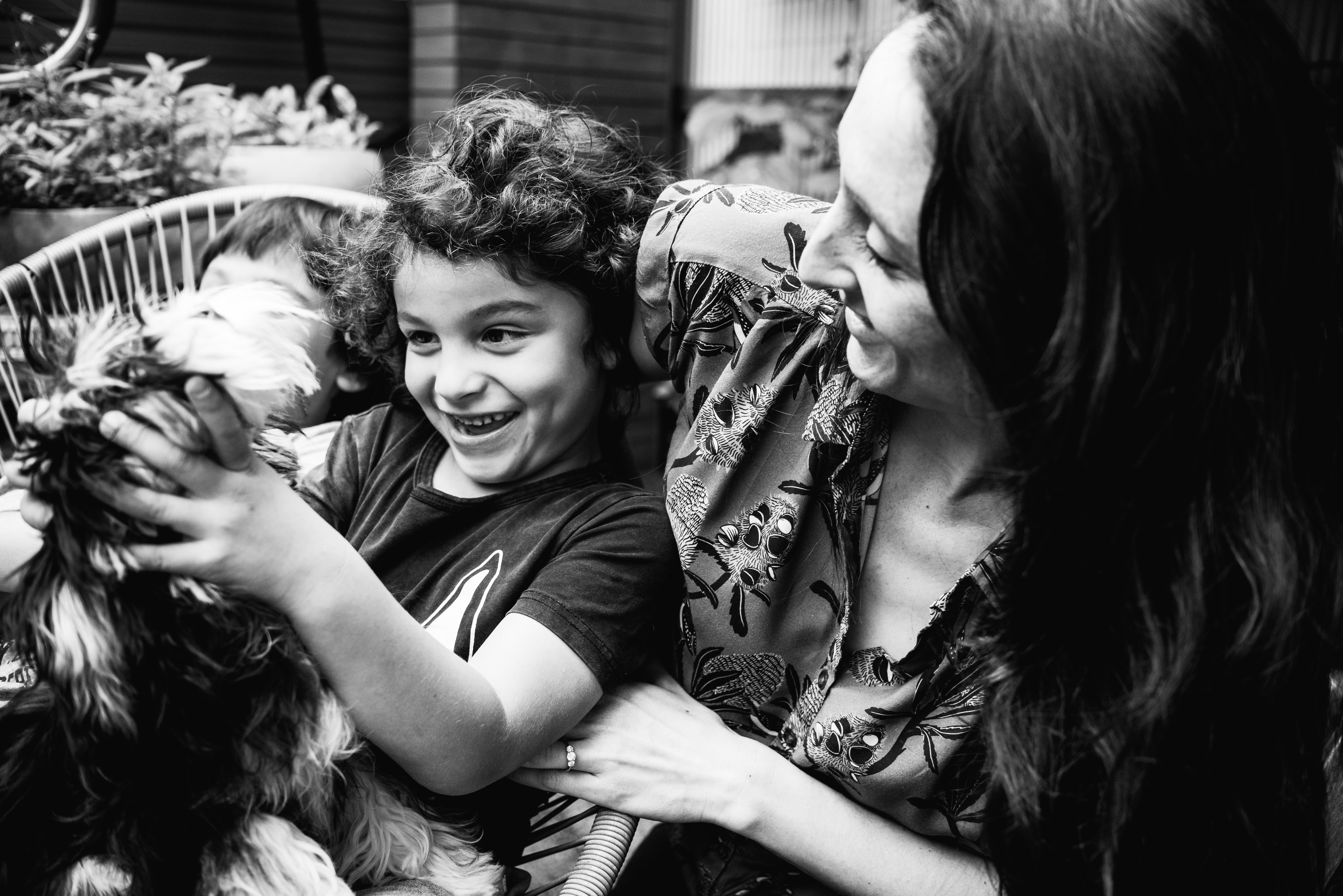 funny photograph of a boy holding his pet dog as his mother watches in Carlton North, Melbourne, Australia