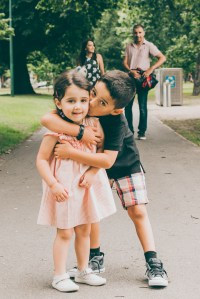 Melbourne Lifestyle family photographer Liyat G Haile documents and captures a happy brother kissing his sister as parents watch in the background at Princes Park, Melbourne, Australia
