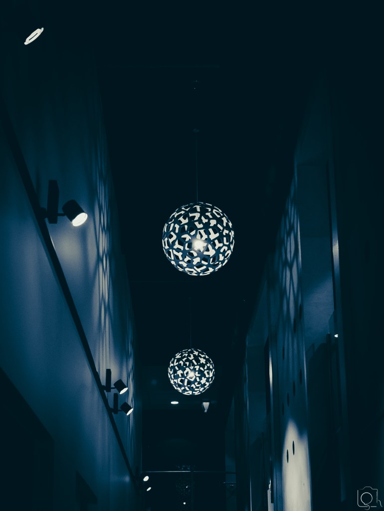 Light globes enclosed inside circular hive-designed surrounding creating shadow patterns on the walls of the building