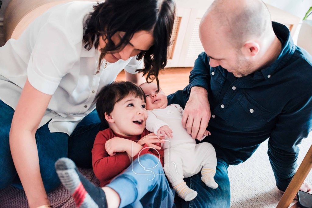 A lifestyle photography session with a Melbourne family in their home. A mother and a father with sitting on their living room floor casually interacting with their son and newborn baby girl. Photograph by Liyat Haile.
