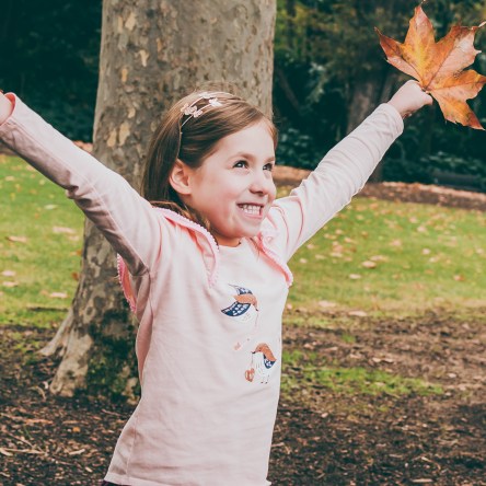 Fun Portrait of a child holding Autumn leaves at Fitzroy Gardens in Melbourne, Australia